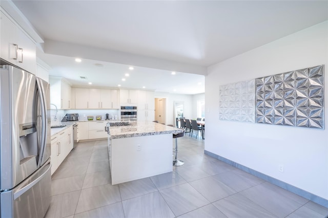 6956 Meadowbriar Ln, Dallas, TX 75230 - kitchen with appliances with stainless steel finishes, a center island, a breakfast bar area, recessed lighting, and white cabinetry