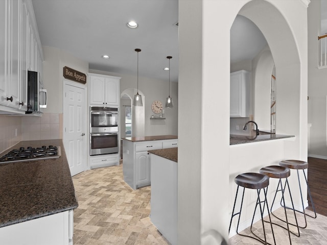 5503 Midnight Moon Dr, Frisco, TX 75036 - kitchen featuring appliances with stainless steel finishes, a peninsula, white cabinetry, tasteful backsplash, and arched walkways