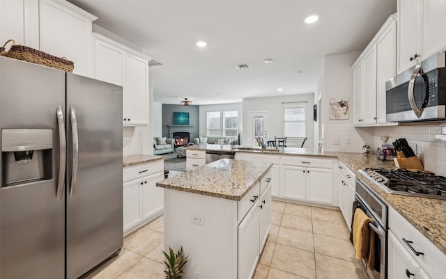 3814 Bastrop St, Melissa, TX 75454 - kitchen with appliances with stainless steel finishes, tasteful backsplash, a peninsula, a lit fireplace, and white cabinetry