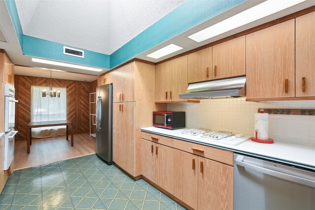 921 Sleepy Hollow Dr, Garland, TX 75043 - kitchen with appliances with stainless steel finishes, under cabinet range hood, light brown cabinets, a chandelier, and a textured ceiling