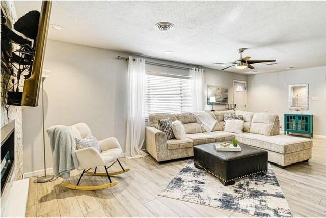 1037 Cavender Dr, Hurst, TX 76053 - living area featuring a textured ceiling, ceiling fan, light wood-style floors, and a fireplace