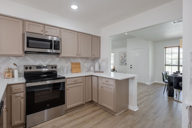 2508 Independence Dr, Mesquite, TX 75150 - kitchen featuring appliances with stainless steel finishes, a peninsula, a textured ceiling, light wood-style flooring, and decorative backsplash