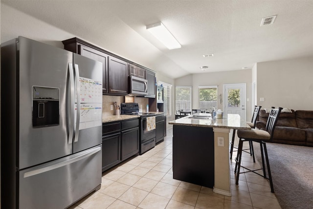 628 Cameron Way, Azle, TX 76020 - kitchen featuring appliances with stainless steel finishes, a breakfast bar area, vaulted ceiling, light stone counters, and an island with sink