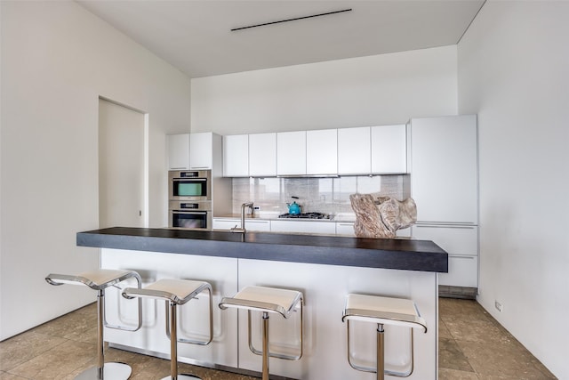1717 Arts Plz Unit 1808, Dallas, TX 75201 - kitchen featuring appliances with stainless steel finishes, dark countertops, a breakfast bar, white cabinetry, and backsplash