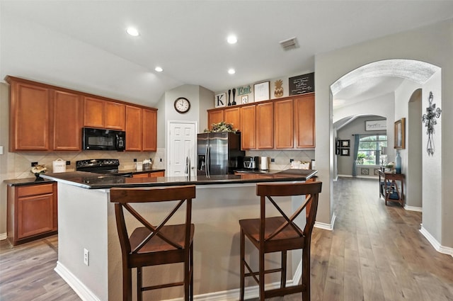 9210 Wild River Dr, Arlington, TX 76002 - kitchen featuring black appliances, arched walkways, dark countertops, light wood-type flooring, and vaulted ceiling