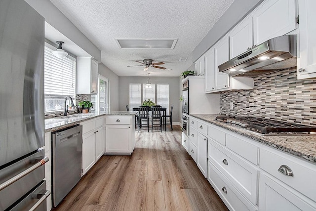 5800 Thoreau Ln, Arlington, TX 76016 - kitchen with stainless steel appliances, under cabinet range hood, a textured ceiling, white cabinets, and wood finished floors