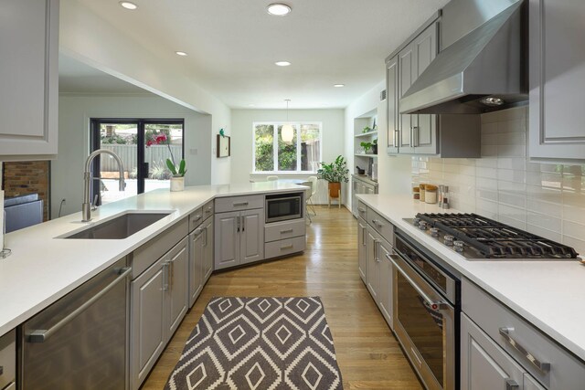4232 Meadowdale Ln, Dallas, TX 75229 - kitchen with appliances with stainless steel finishes, wall chimney exhaust hood, gray cabinetry, wood finished floors, and backsplash