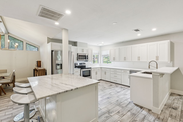 6010 Preston Creek Dr, Dallas, TX 75240 - kitchen featuring appliances with stainless steel finishes, a breakfast bar area, a peninsula, wood finish floors, and white cabinets