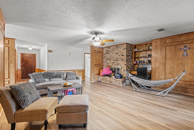 567 Celtic Rd, Howe, TX 75459 - living area with a ceiling fan, light wood finished floors, wooden walls, a fireplace, and a textured ceiling