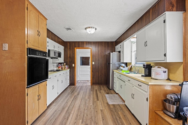 567 Celtic Rd, Howe, TX 75459 - kitchen featuring stainless steel appliances, light countertops, light wood-type flooring, a textured ceiling, and wooden walls
