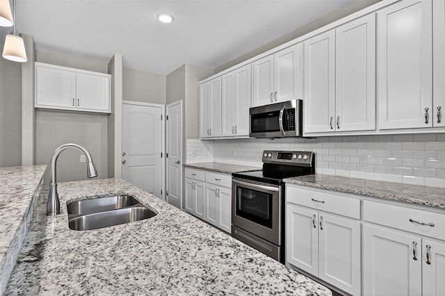 515 W Broad St, Pilot Point, TX 76258 - kitchen featuring appliances with stainless steel finishes, decorative backsplash, light stone countertops, white cabinets, and decorative light fixtures