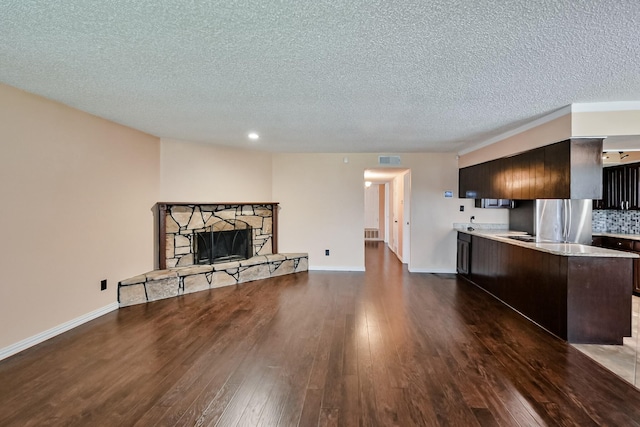 914 Highcrest Dr, Arlington, TX 76017 - unfurnished living room featuring dark wood-style floors, a textured ceiling, a stone fireplace, and recessed lighting
