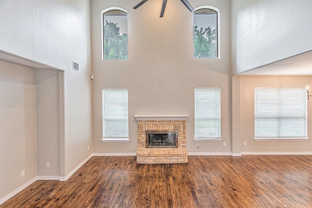 1900 Sumac Dr, Flower Mound, TX 75028 - unfurnished living room featuring a towering ceiling, a ceiling fan, wood finished floors, a brick fireplace, and healthy amount of natural light