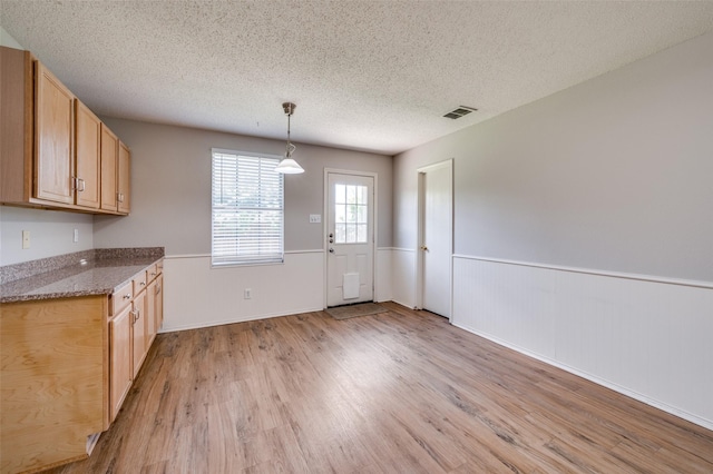 1640 Fieldstone Dr, Little Elm, TX 75068 - unfurnished dining area with a wainscoted wall, light wood-style flooring, and a textured ceiling