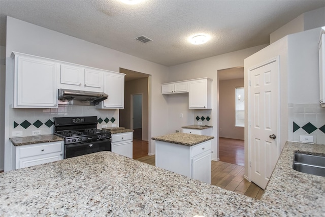 738 Opal Ln, Mesquite, TX 75149 - kitchen with black gas range, under cabinet range hood, light wood-style flooring, tasteful backsplash, and white cabinets