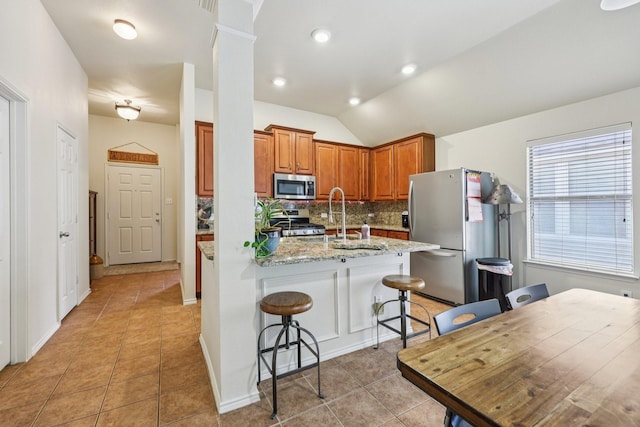 504 Lake Point Dr, Little Elm, TX 75068 - kitchen featuring appliances with stainless steel finishes, brown cabinetry, decorative backsplash, light tile patterned floors, and lofted ceiling