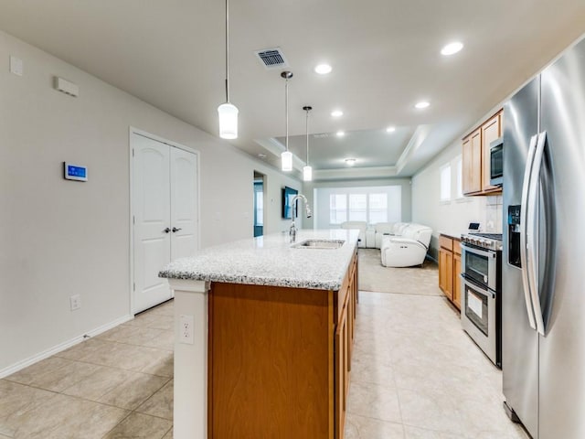 1244 Eagle Ln, Little Elm, TX 76227 - kitchen featuring stainless steel appliances, open floor plan, a raised ceiling, an island with sink, and brown cabinetry