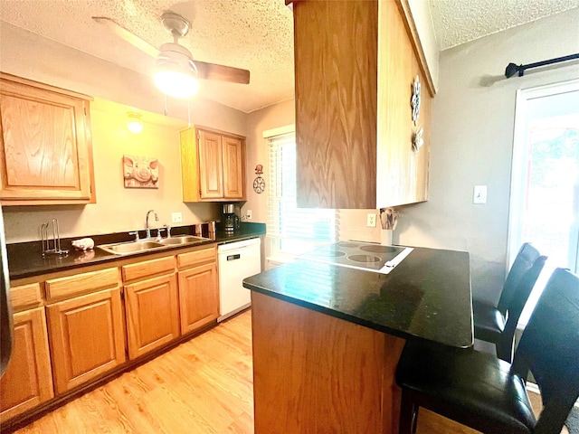 309 Bellaire Dr, Denton, TX 76209 - kitchen featuring dishwasher, a textured ceiling, dark countertops, a kitchen breakfast bar, and light wood finished floors