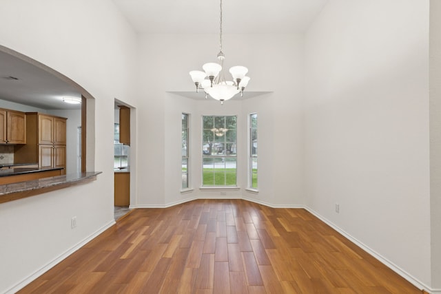 2521 Misty Glen Dr, Flower Mound, TX 75028 - unfurnished dining area with a chandelier, wood finished floors, arched walkways, and a towering ceiling