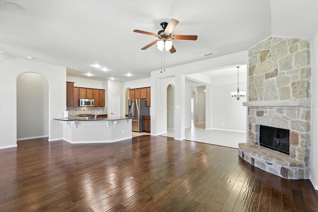 4000 Barnhill Ct, Denton, TX 76208 - unfurnished living room with arched walkways, ceiling fan, dark wood-style flooring, a stone fireplace, and a chandelier