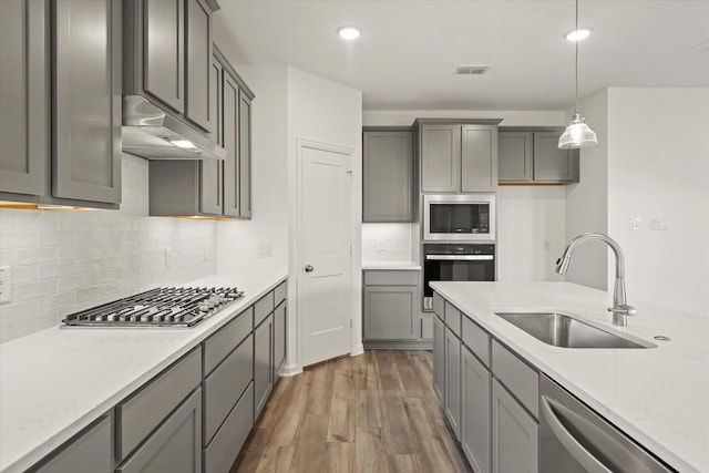 1900 Twisted Tree Ln, Mesquite, TX 75181 - kitchen with appliances with stainless steel finishes, under cabinet range hood, dark wood-style floors, hanging light fixtures, and decorative backsplash