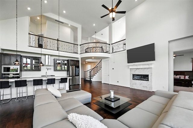 1018 Cascading Creek Dr, Rockwall, TX 75087 - living area with a ceiling fan, dark wood-type flooring, a towering ceiling, stairway, and a fireplace