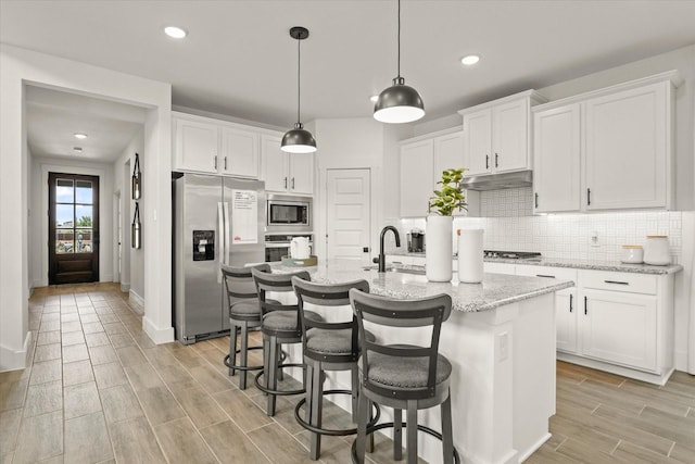 2100 Jade Forest Ln, Mesquite, TX 75181 - kitchen featuring stainless steel appliances, white cabinets, wood tiled floors, decorative backsplash, and an island with sink