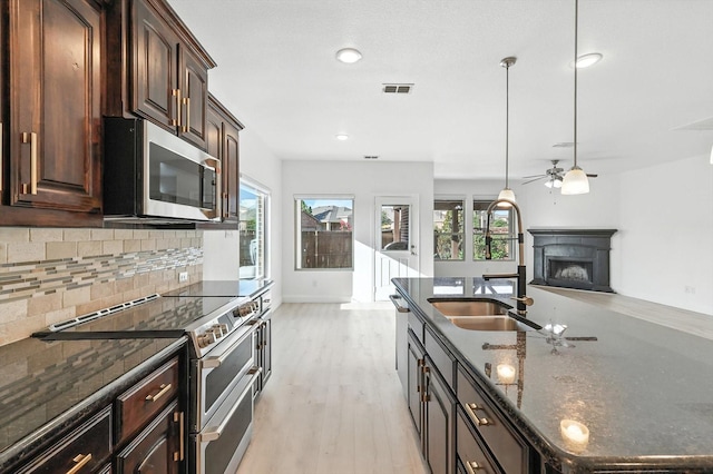 3901 Tule Ranch Rd, Fort Worth, TX 76262 - kitchen featuring stainless steel appliances, a fireplace, tasteful backsplash, an island with sink, and light wood finished floors