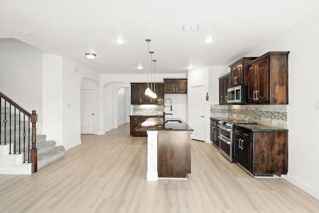 3901 Tule Ranch Rd, Fort Worth, TX 76262 - kitchen featuring stainless steel appliances, dark countertops, arched walkways, light wood-style flooring, and recessed lighting