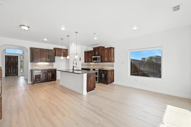 3901 Tule Ranch Rd, Fort Worth, TX 76262 - kitchen featuring appliances with stainless steel finishes, backsplash, light wood-style floors, arched walkways, and dark countertops