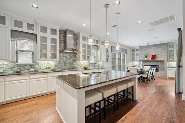 4652 Man O War Rd, Carrollton, TX 75010 - kitchen featuring wall chimney range hood, a kitchen bar, backsplash, dark stone countertops, and light wood-style floors