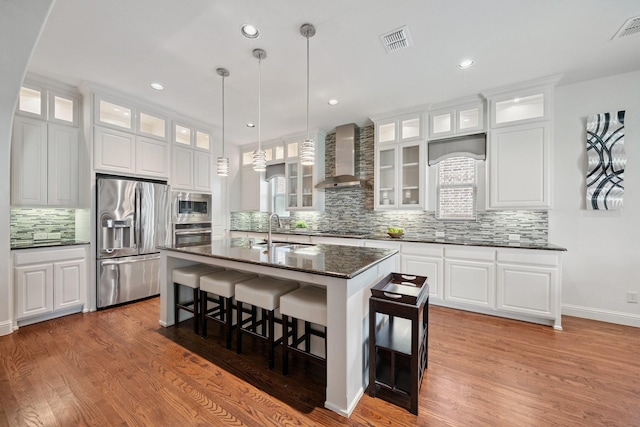 4652 Man O War Rd, Carrollton, TX 75010 - kitchen featuring appliances with stainless steel finishes, wall chimney exhaust hood, tasteful backsplash, a kitchen breakfast bar, and wood finished floors
