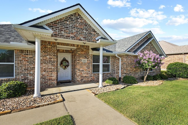 102 Southfork Cir, Pottsboro, TX 75076 - view of exterior entry with brick siding, a yard, and roof with shingles