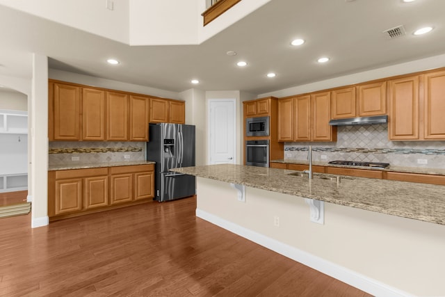 4560 Cheetah Trl, Frisco, TX 75034 - kitchen featuring appliances with stainless steel finishes, under cabinet range hood, tasteful backsplash, light stone counters, and a kitchen breakfast bar