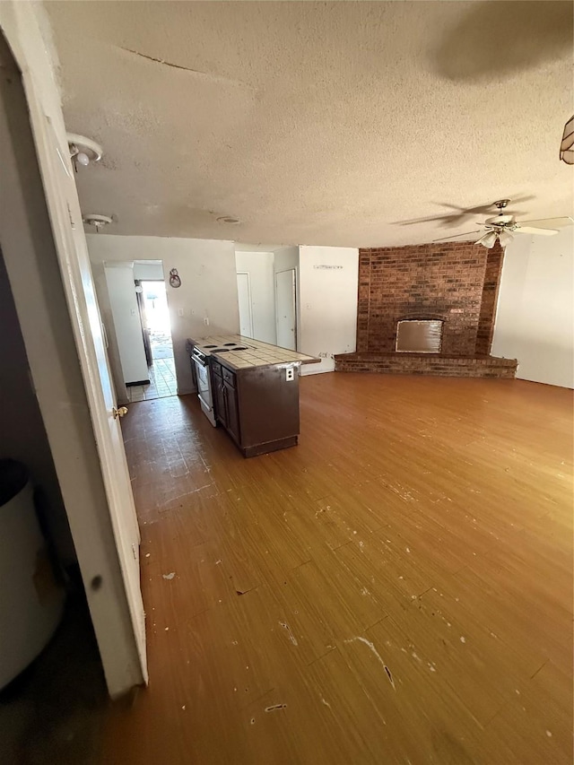 5918 Highcrest Dr, Garland, TX 75043 - unfurnished living room featuring wood finished floors, a textured ceiling, ceiling fan, and a brick fireplace