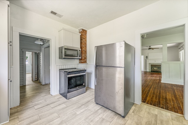 1143 W Jones St, Stephenville, TX 76401 - kitchen featuring appliances with stainless steel finishes, ceiling fan, a fireplace, white cabinetry, and light wood-style floors