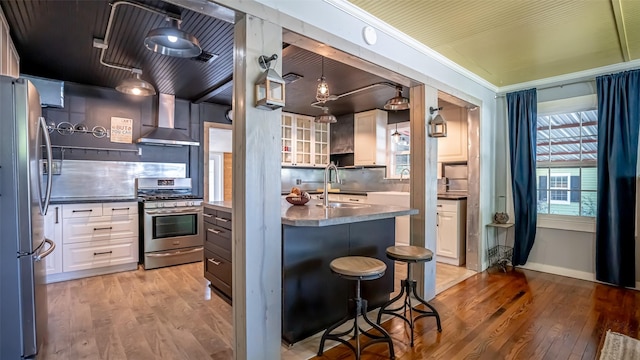 1250 N Isla St, Stephenville, TX 76401 - kitchen featuring stainless steel appliances, wall chimney exhaust hood, light wood-style flooring, and white cabinetry