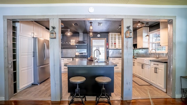 1250 N Isla St, Stephenville, TX 76401 - kitchen with appliances with stainless steel finishes, wall chimney range hood, a kitchen island with sink, white cabinets, and tasteful backsplash