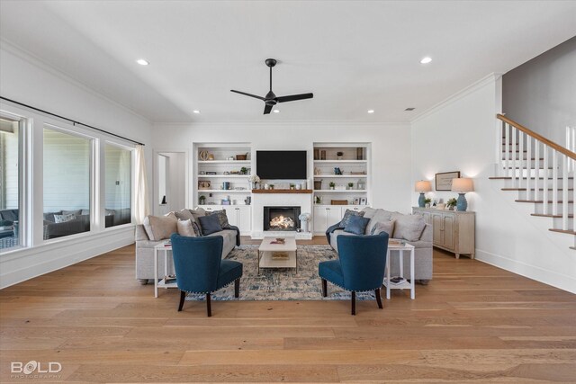 10946 Whispering Path Dr, Shreveport, LA 71106 - living area featuring a ceiling fan, ornamental molding, stairs, light wood-type flooring, and a warm lit fireplace