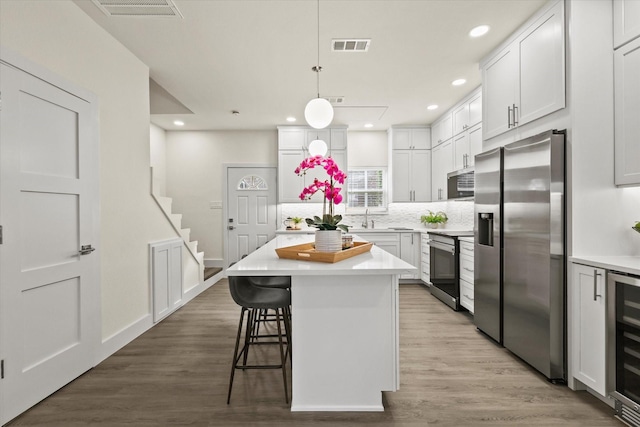 2727 Shelby Ave Unit O, Dallas, TX 75219 - kitchen featuring appliances with stainless steel finishes, light countertops, wood finished floors, decorative backsplash, and a breakfast bar