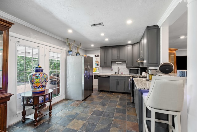 6301 Shadydell Dr, Fort Worth, TX 76135 - kitchen featuring appliances with stainless steel finishes, gray cabinetry, ornamental molding, decorative backsplash, and light stone counters