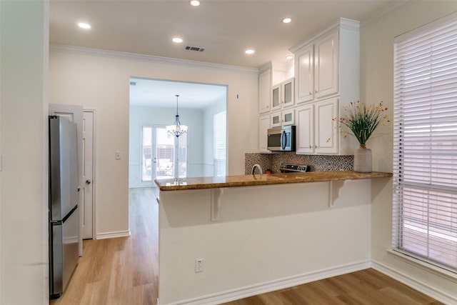 661 Raintree Cir, Coppell, TX 75019 - kitchen with appliances with stainless steel finishes, light wood finished floors, white cabinetry, a kitchen breakfast bar, and crown molding
