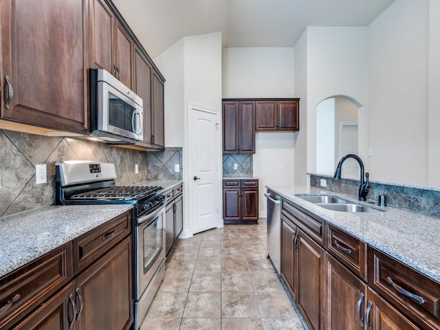 7425 Ty Cir, Mckinney, TX 75072 - kitchen with appliances with stainless steel finishes, light stone countertops, tasteful backsplash, arched walkways, and dark brown cabinetry