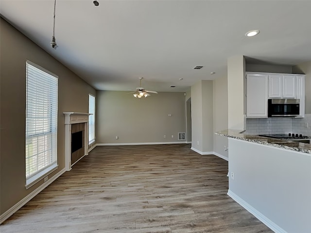 2829 Alcot Ln, Grand Prairie, TX 75052 - kitchen featuring stainless steel microwave, a fireplace, ceiling fan, white cabinetry, and decorative backsplash