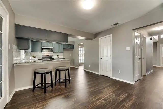 4914 Redwater Dr, Arlington, TX 76018 - kitchen with stainless steel appliances, a peninsula, a breakfast bar area, and dark wood-type flooring