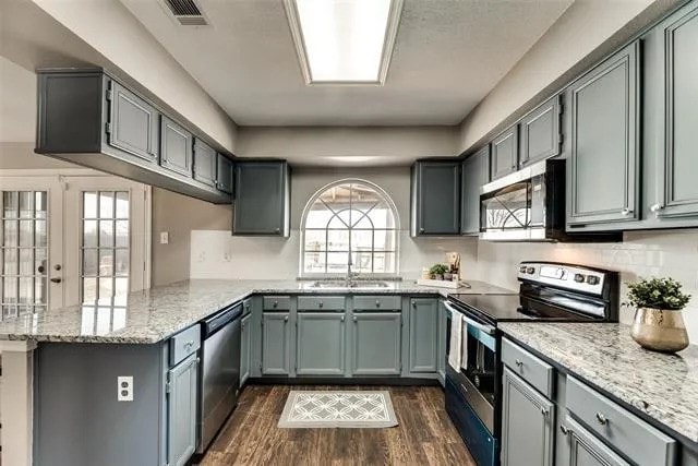 4914 Redwater Dr, Arlington, TX 76018 - kitchen with appliances with stainless steel finishes, a peninsula, dark wood-style floors, light stone countertops, and gray cabinets