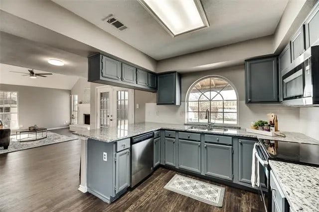 4914 Redwater Dr, Arlington, TX 76018 - kitchen featuring stainless steel appliances, open floor plan, a peninsula, dark wood-type flooring, and light stone counters