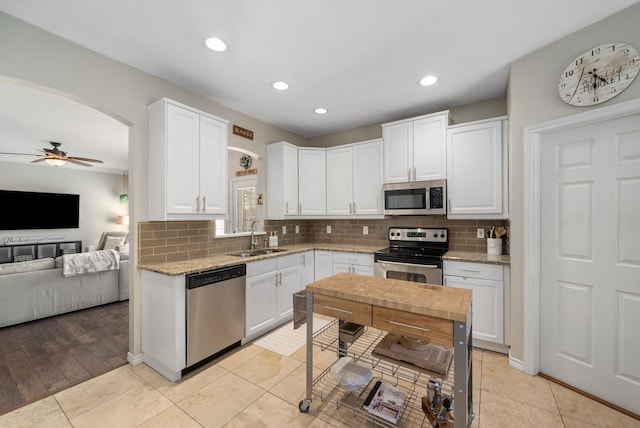 8571 Hidden Spring Dr, Frisco, TX 75034 - kitchen featuring appliances with stainless steel finishes, arched walkways, ceiling fan, tasteful backsplash, and white cabinets