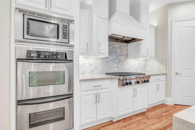 11334 Graceland Ln, Frisco, TX 75033 - kitchen featuring stainless steel appliances, custom exhaust hood, light wood-type flooring, light countertops, and white cabinets