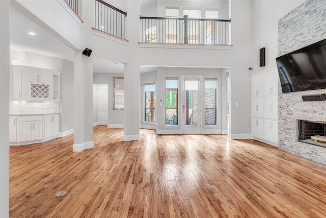 11334 Graceland Ln, Frisco, TX 75033 - unfurnished living room with light wood-style flooring, a stone fireplace, and a towering ceiling